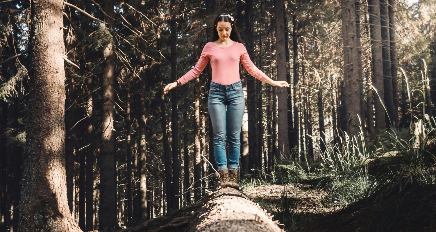Femme en équilibre sur un tronc d'arbre. Elle est dans une forêt.